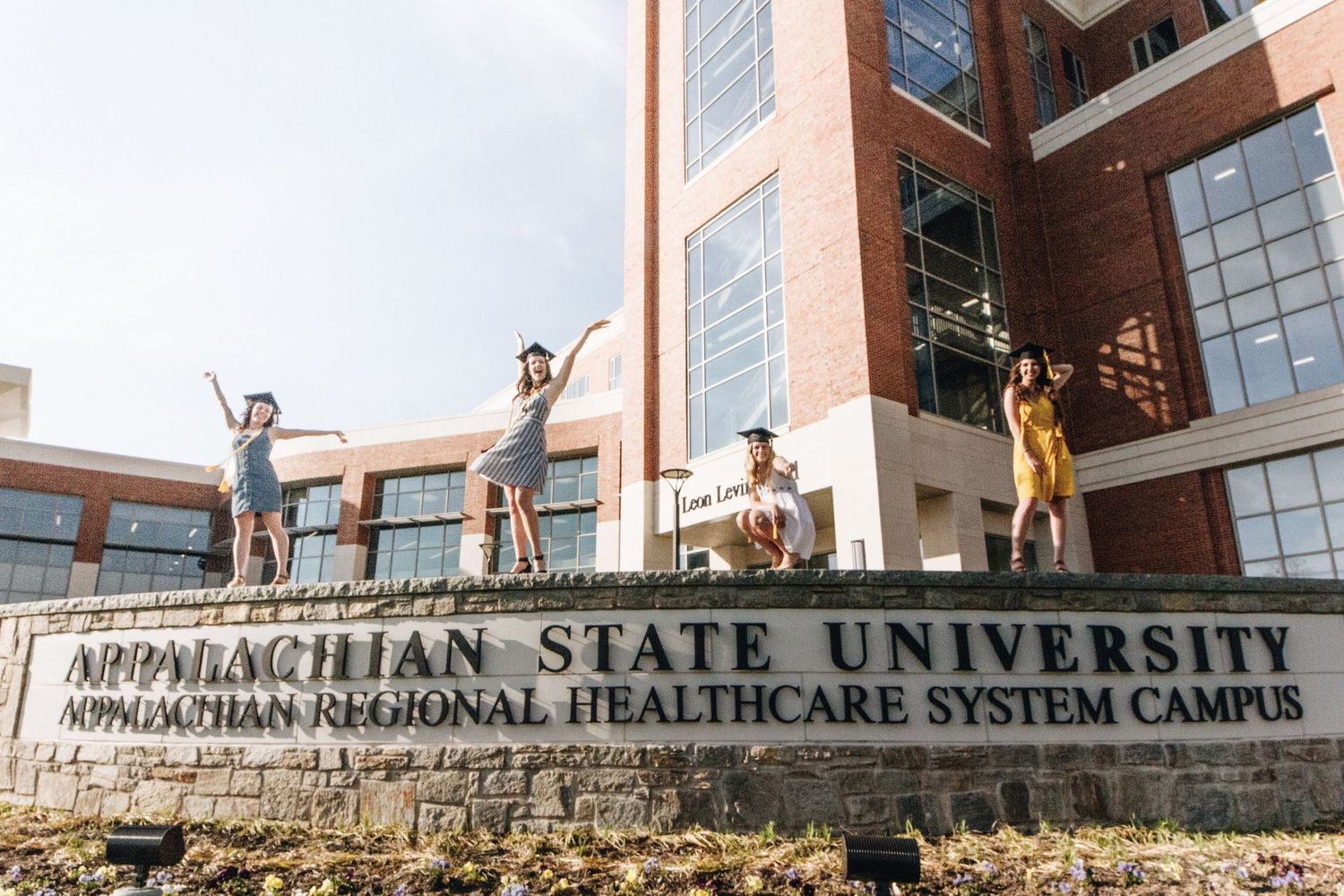 People posing joyfully in front of Appalachian State University Healthcare System Campus sign.