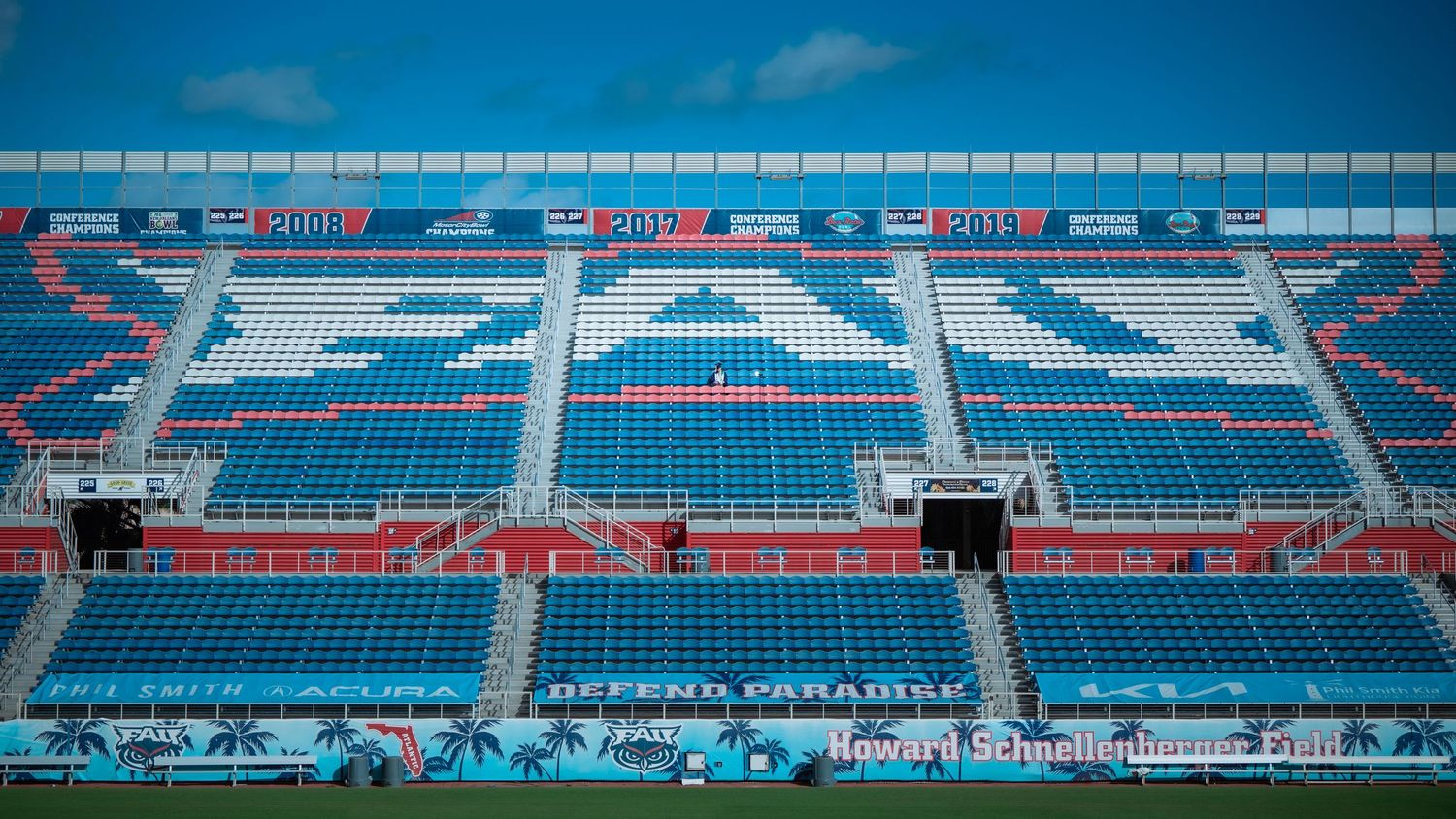 Stadium seating with blue and white seats under bright sky at FAU stadium.