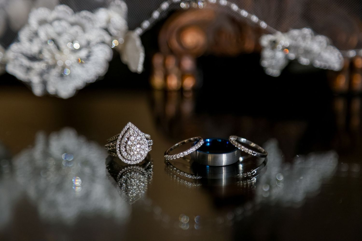 Close-up shot of a sparkling diamond engagement ring and wedding band with delicate lace details in the background.