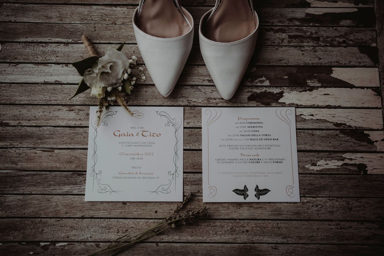 Wedding invitations and white bridal shoes arranged on rustic wooden planks.