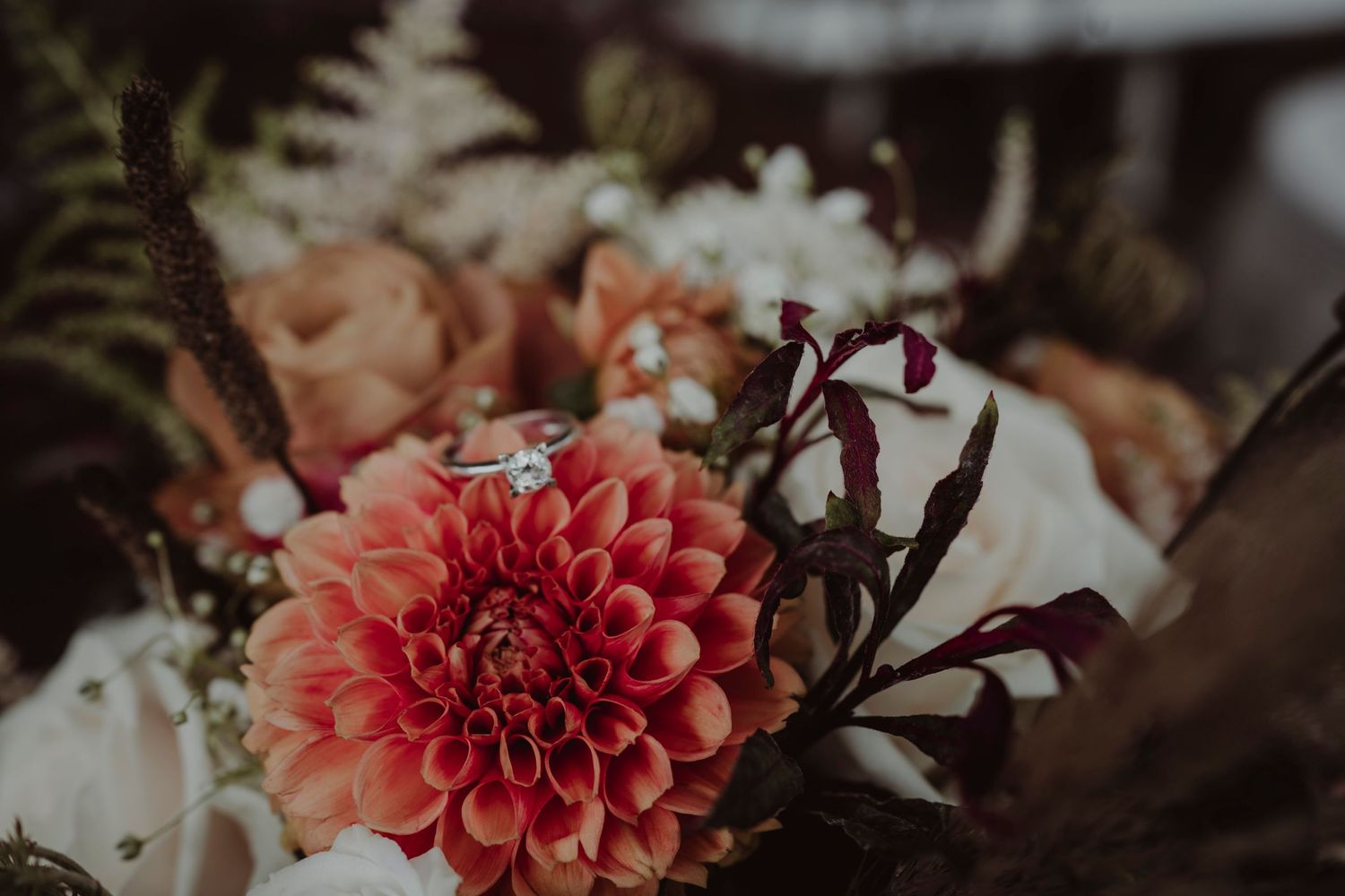 Close-up of pink dahlia in romantic wedding bouquet with ferns and white flowers.