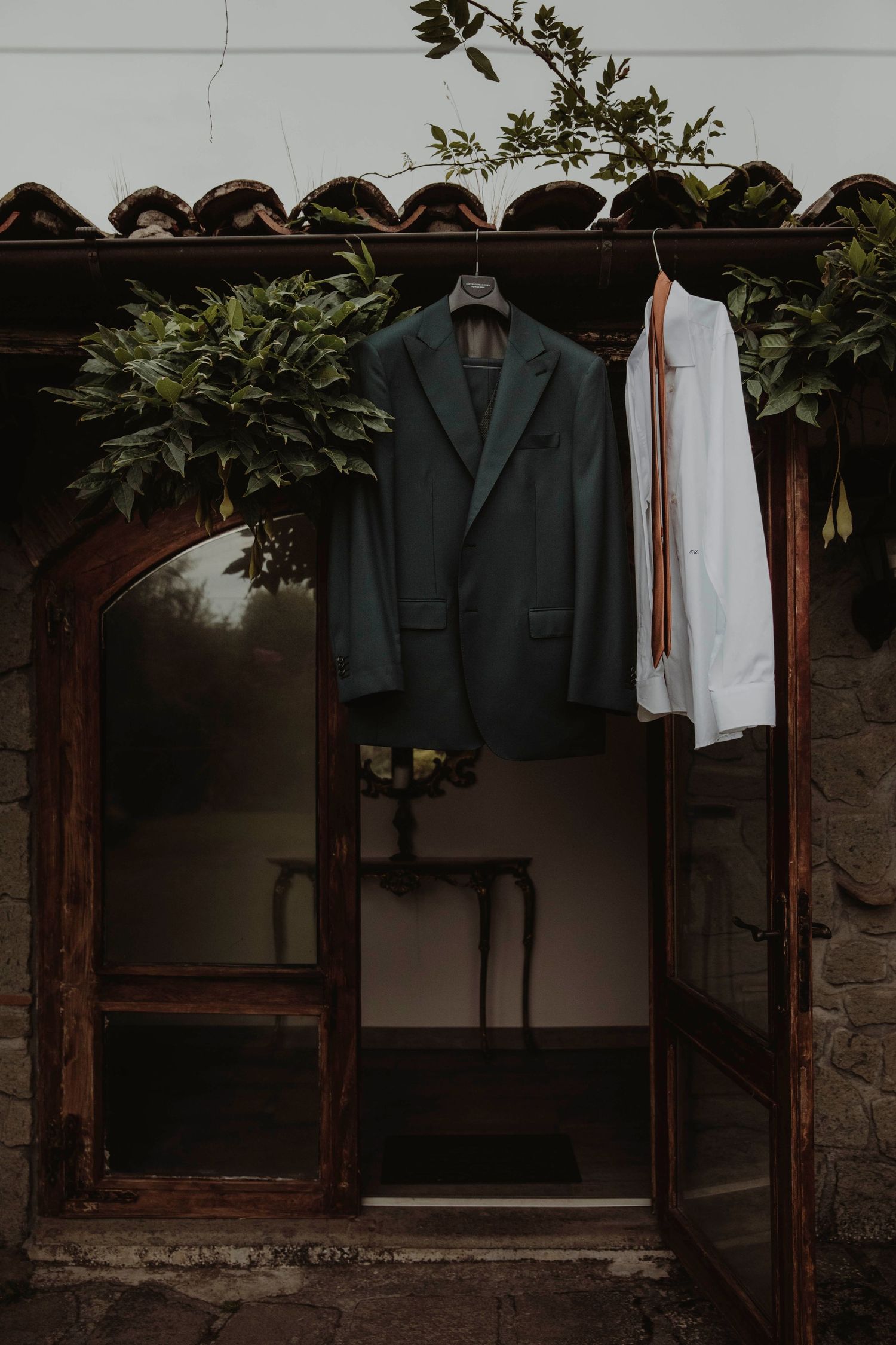 Dark formal suit displayed in stone-framed doorway with natural foliage decoration.