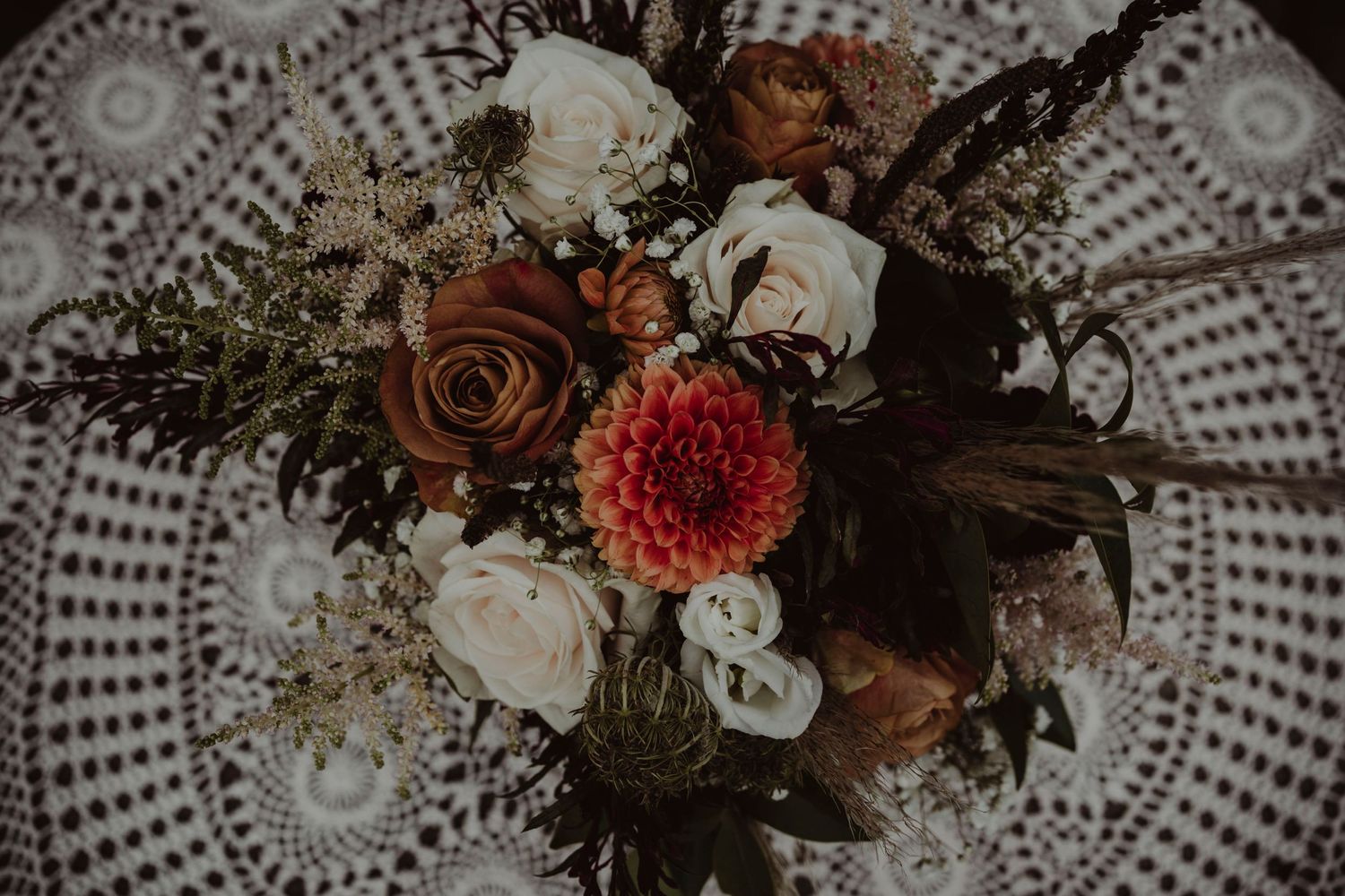 Wedding bouquet with red and white flowers arranged on delicate lace doily from above.