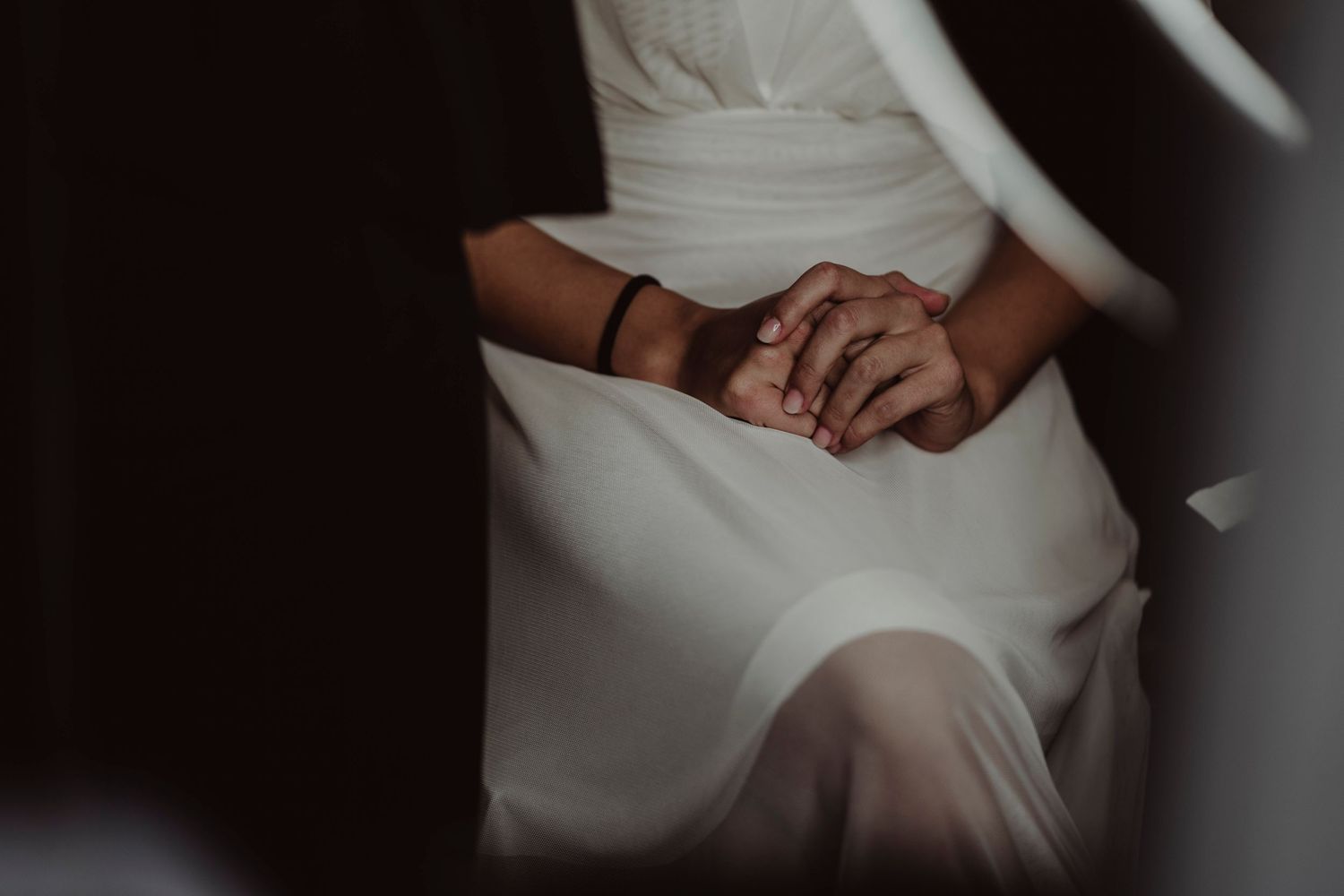 Close-up of hands clasped together against flowing white fabric.
