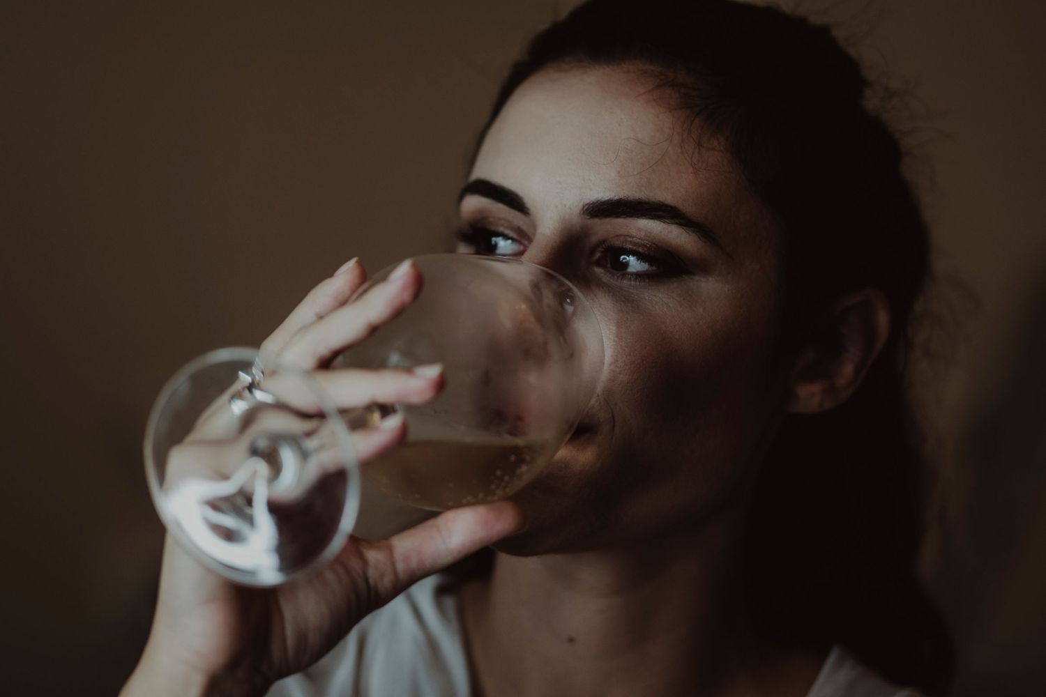 Dramatic portrait of someone sipping from a wine glass in moody lighting.