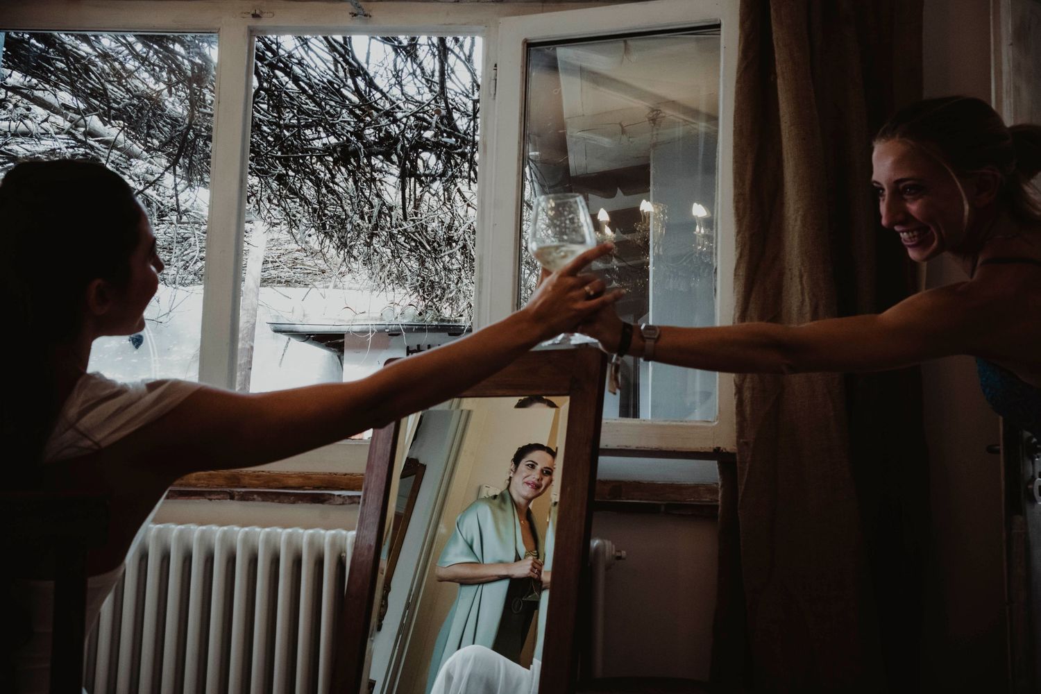 Two figures toast champagne glasses in front of a window with natural lighting.