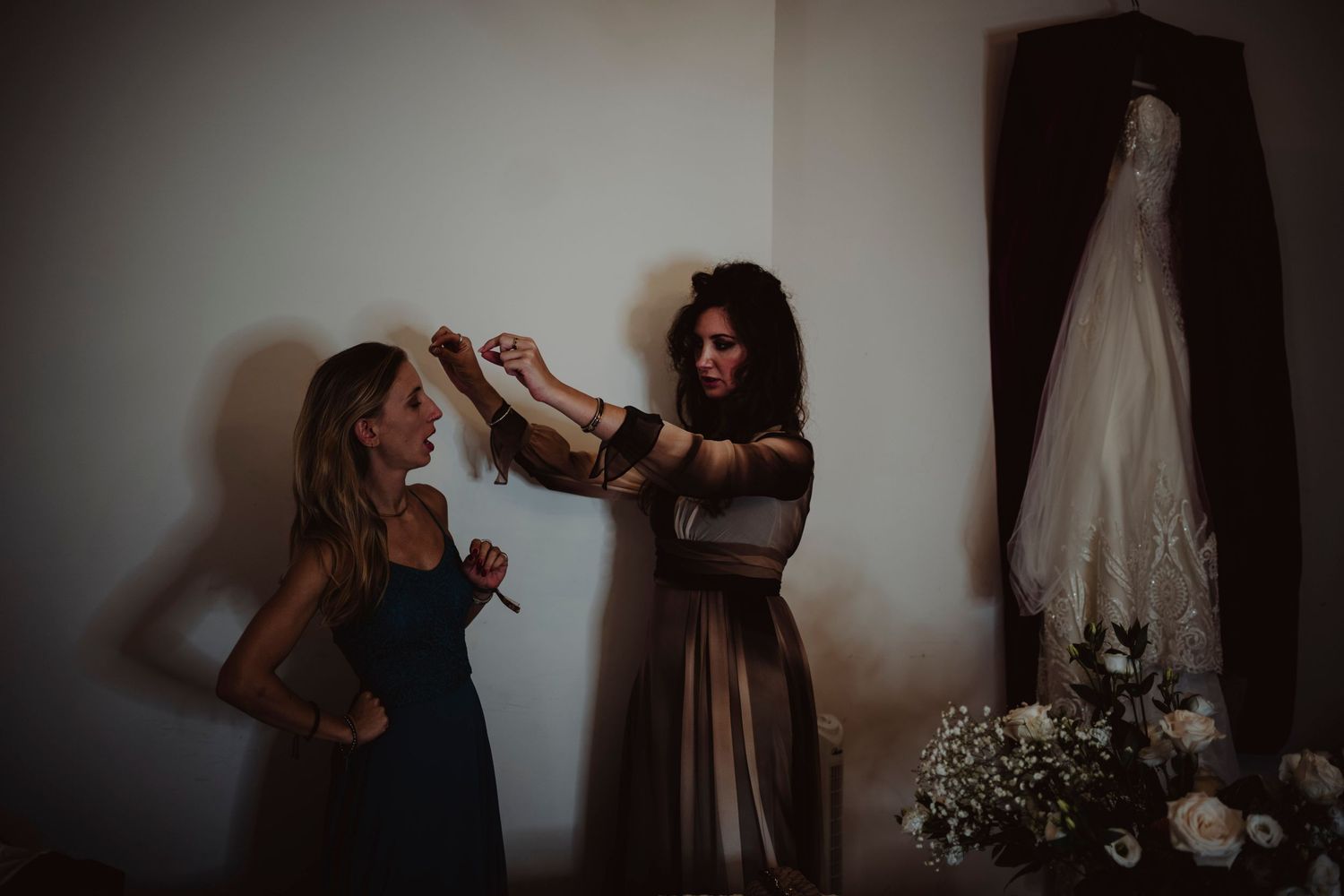 Wedding preparations show two people getting ready with a white dress hanging in background.