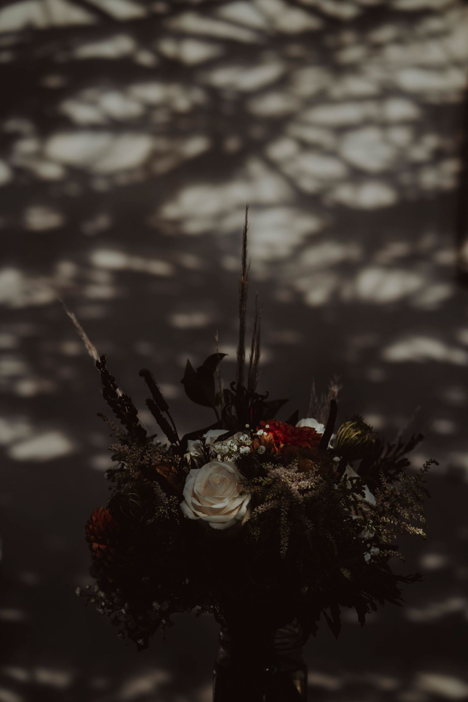 Dark moody floral arrangement with white roses and red flowers casting dramatic shadows on the wall.