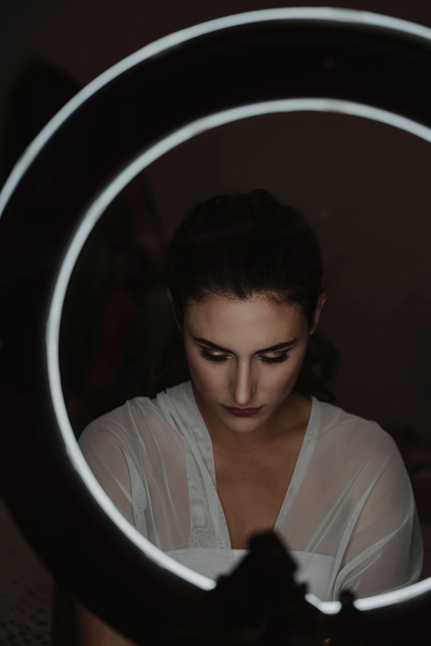 Dramatic ring light portrait creates striking shadows during bridal preparation.