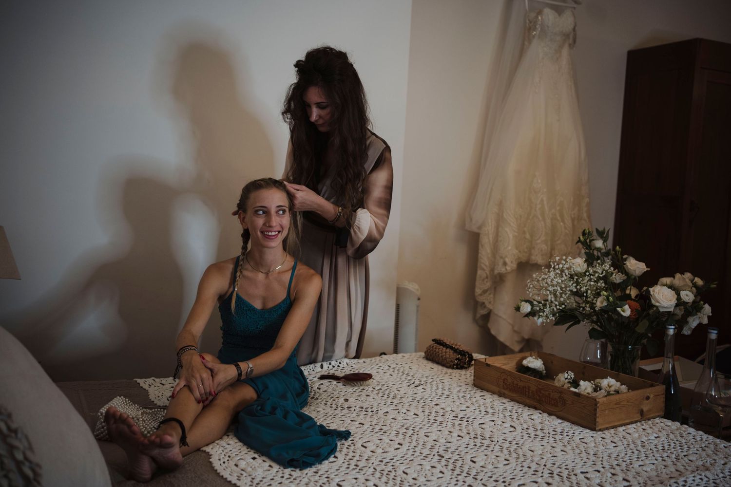 Two people getting ready in a room with a wedding dress visible in the background.