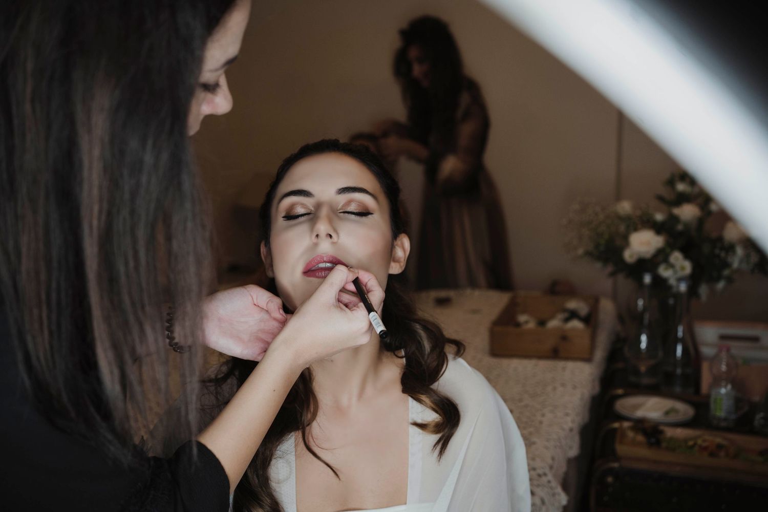Professional makeup artist applies lipstick during bridal preparation.