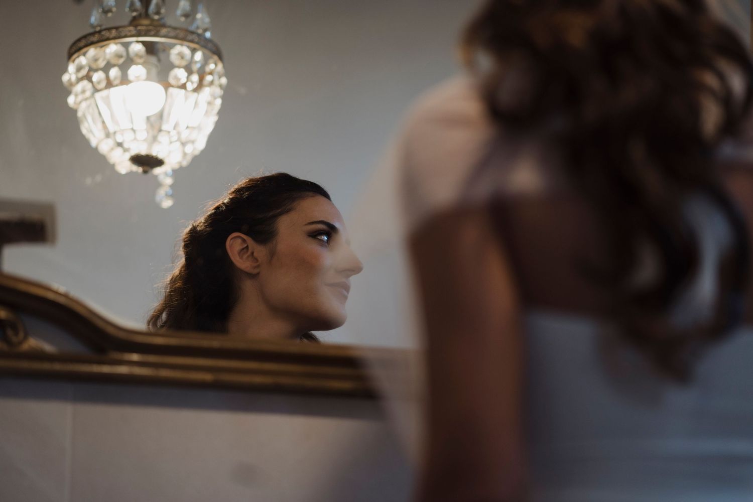 Reflection in an ornate mirror under a crystal chandelier in an elegant room.