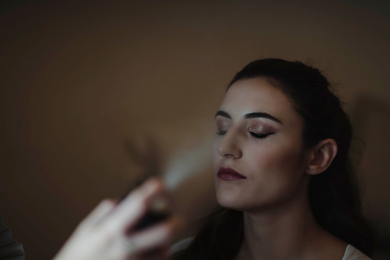Close-up shot of professional bridal makeup application in dim atmospheric lighting.