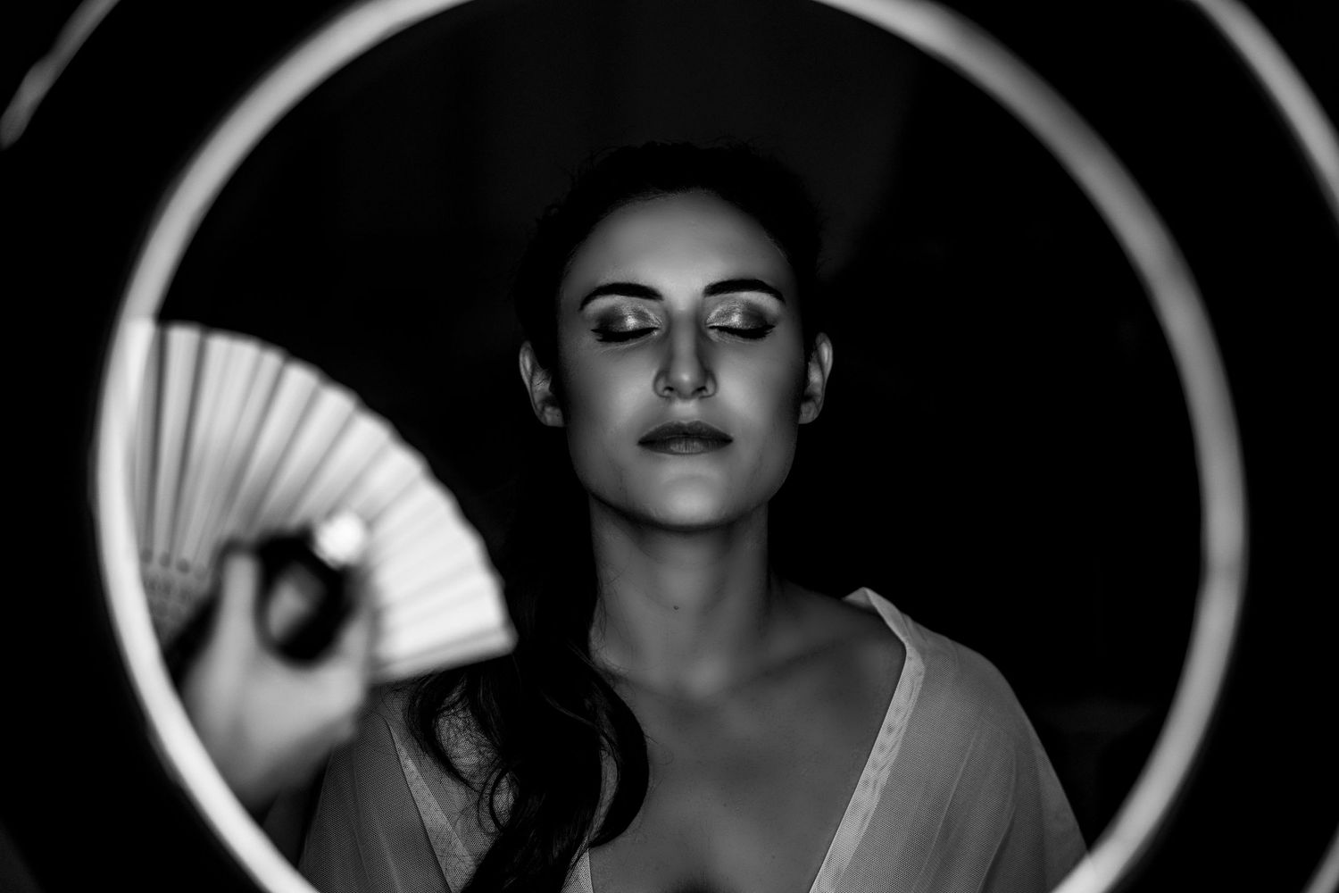Artistic black and white portrait of a woman holding a decorative fan against a circular backdrop.