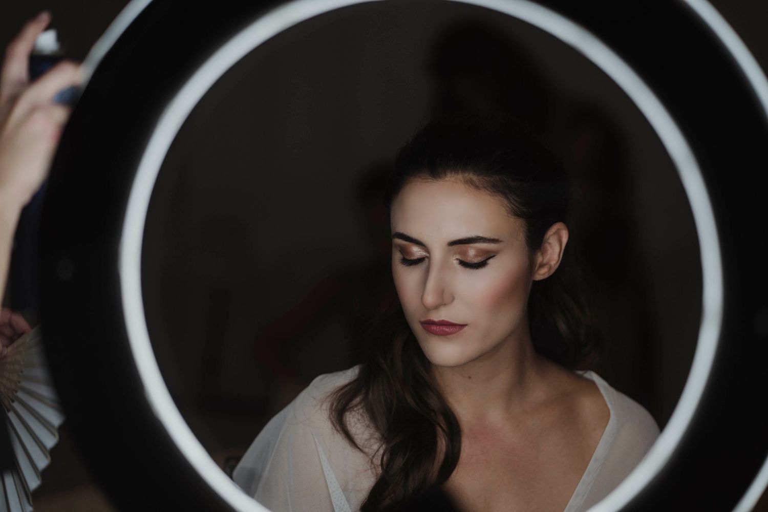 Ring light illuminates a dramatic bridal makeup session with moody lighting and soft shadows.