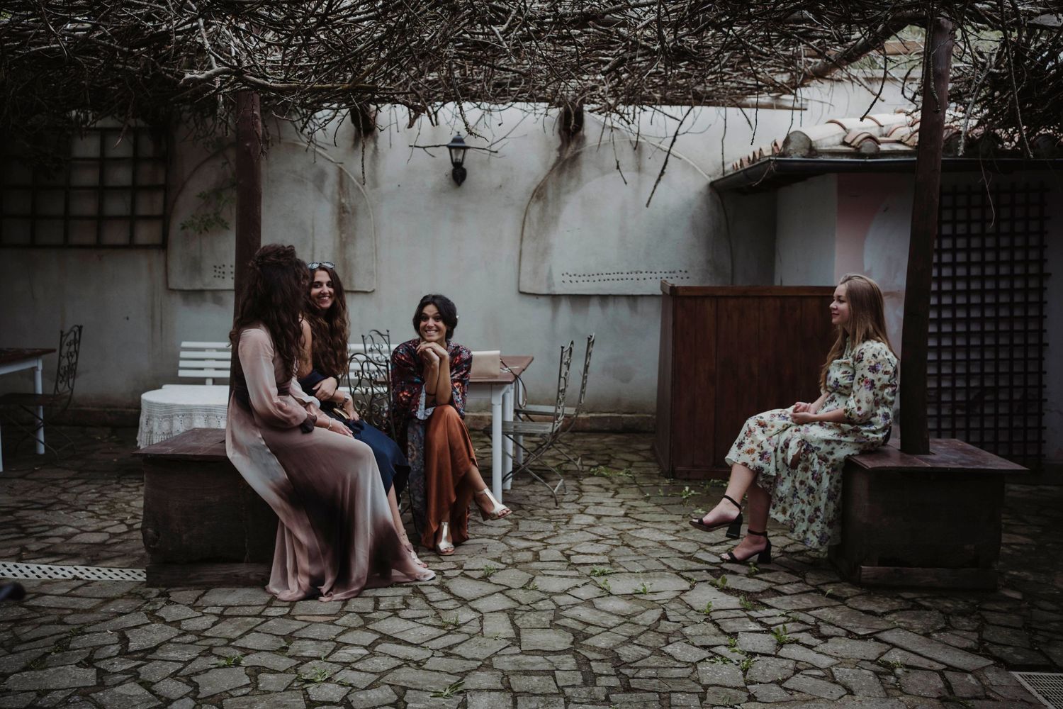 People sitting together in an outdoor courtyard with stone pavement and rustic walls.