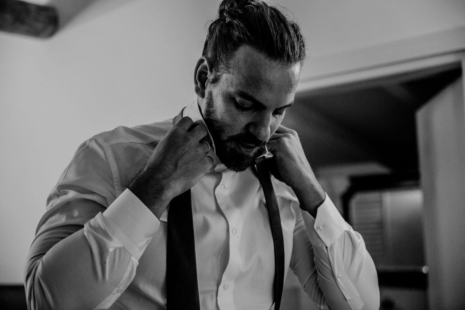 Black and white portrait of someone adjusting a bowtie while wearing a formal white shirt and black tie.
