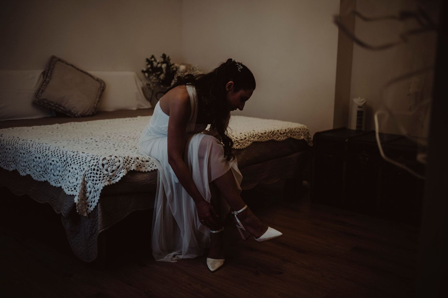 Wedding preparation moment as someone puts on shoes in a dimly lit room.