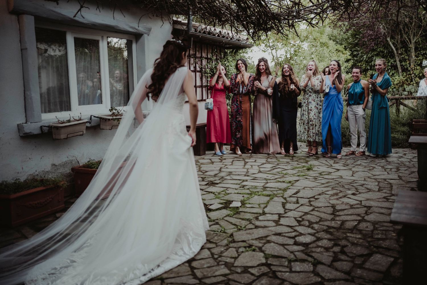 Wedding guests watching as bride in flowing white dress walks on stone pathway.