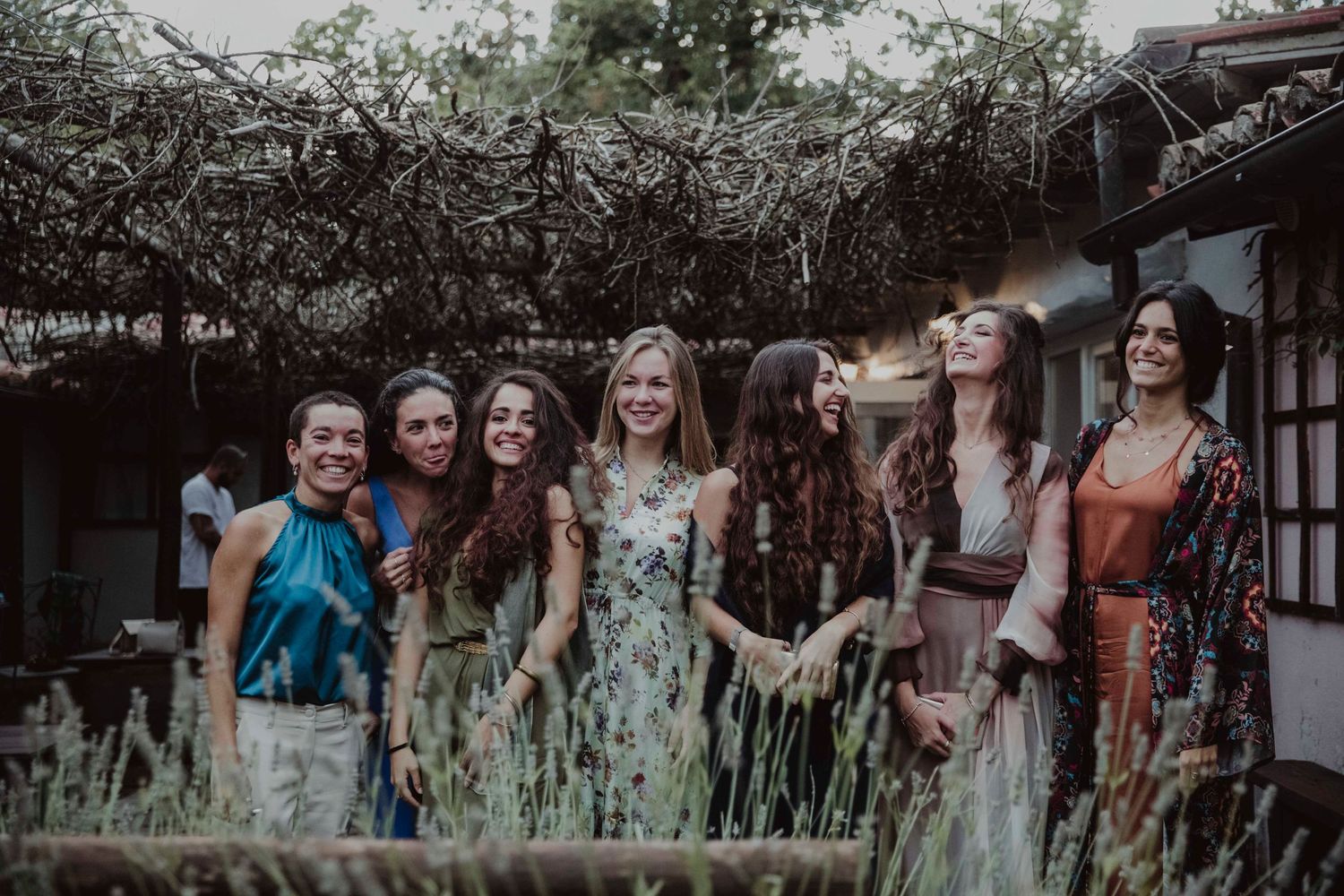 Group of wedding guests in colorful dresses standing together in a garden setting.