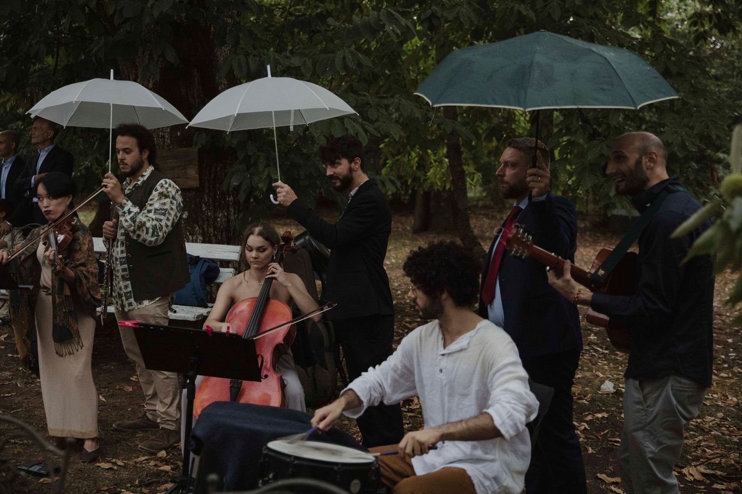 Musicians with umbrellas perform during an outdoor wedding ceremony.