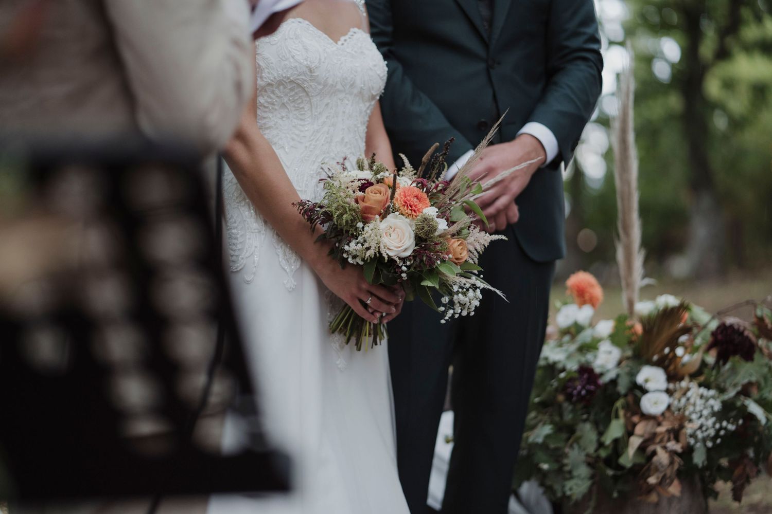 Close-up of couple holding wedding bouquet with white and peach flowers against formal attire.