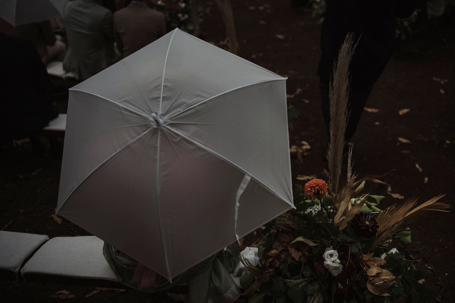White umbrella against dark background with floral decorations at outdoor wedding setting.