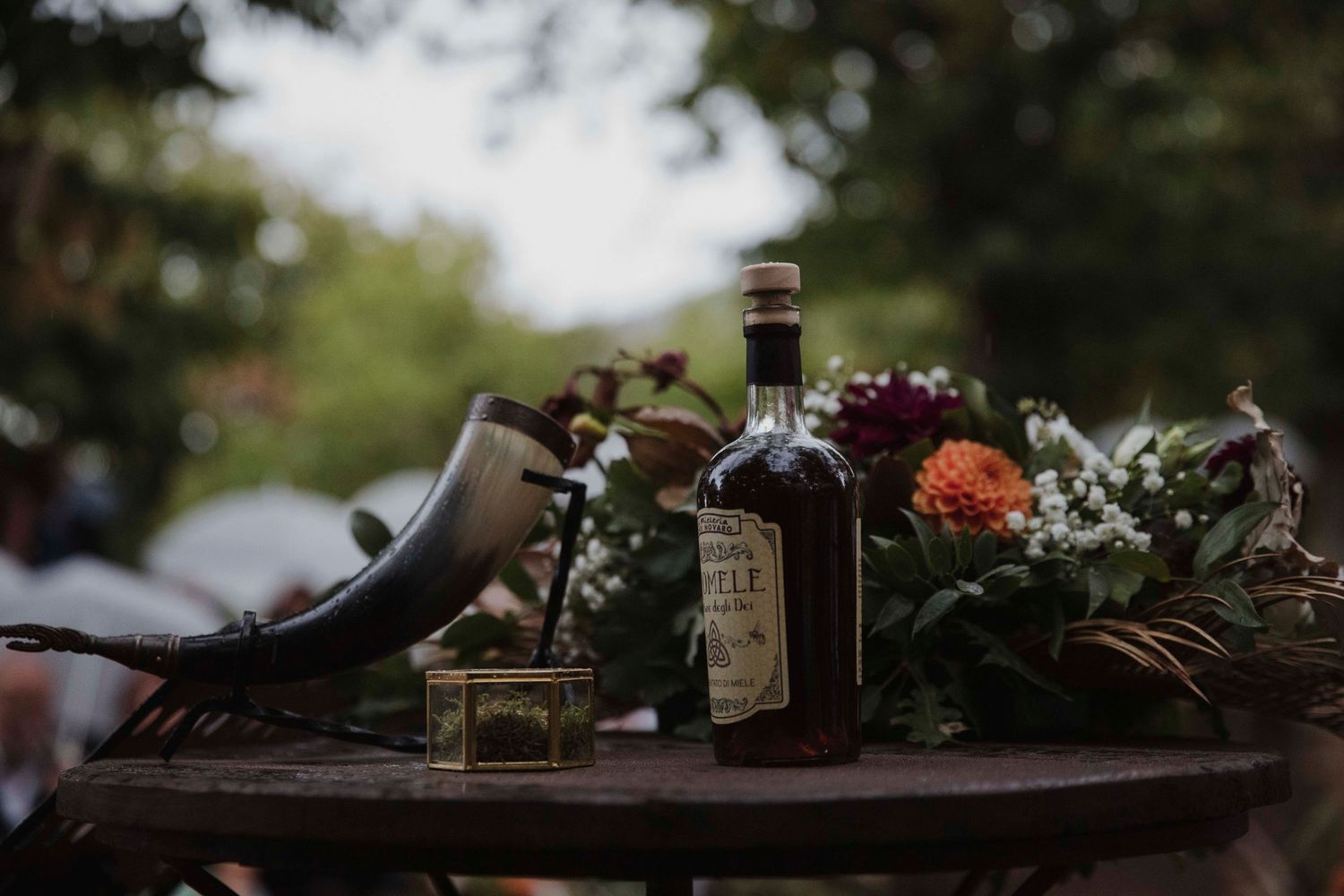Decorative bottles and floral arrangements adorn a rustic wooden table at an outdoor wedding reception.