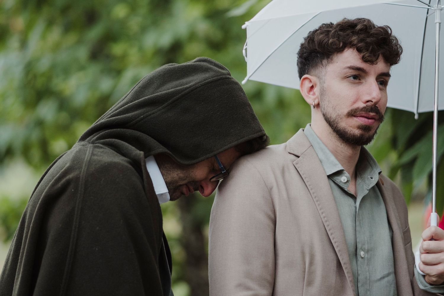 Two guests stand under umbrellas at an outdoor event.