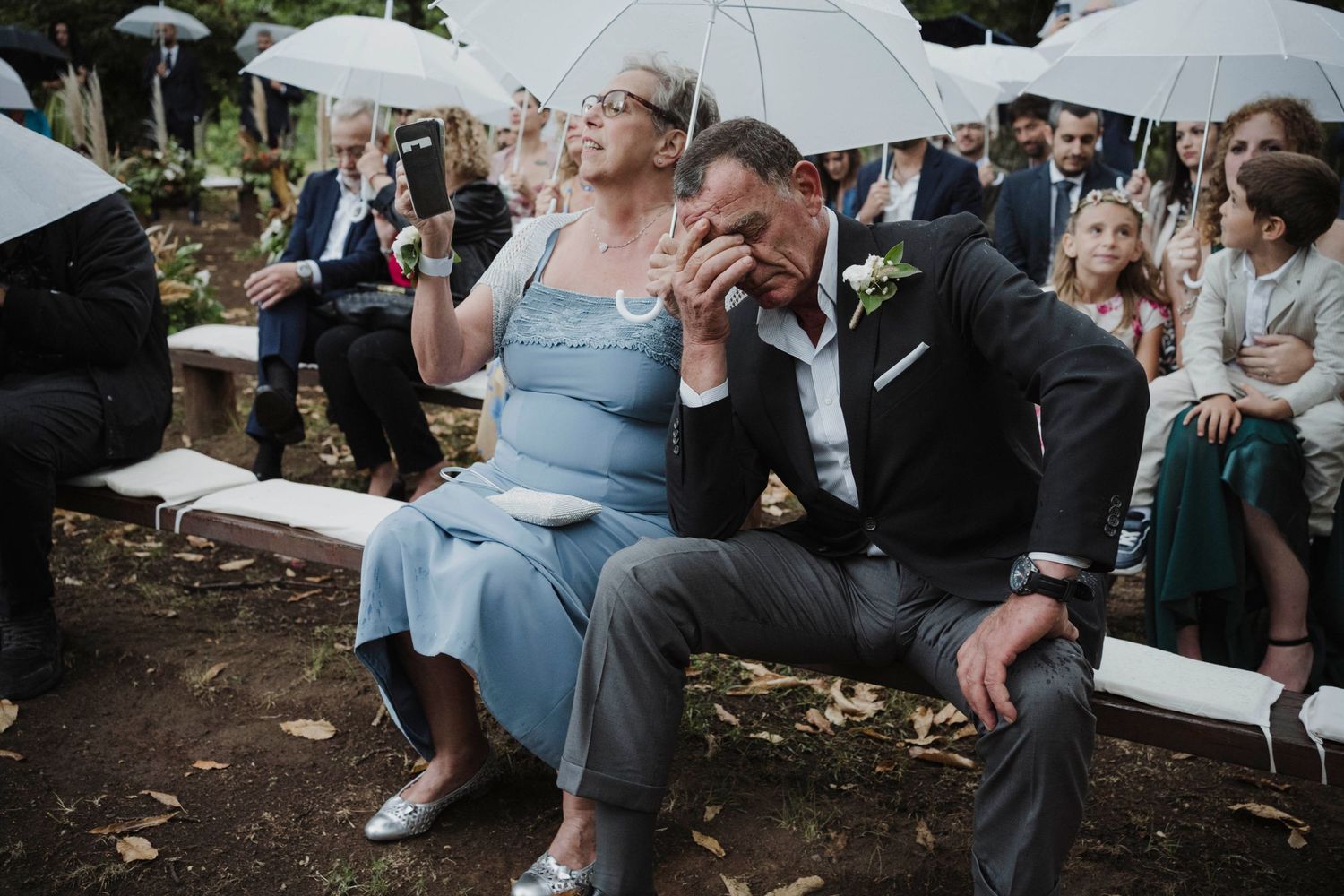 Wedding guests share a lighthearted moment while seated with umbrellas.