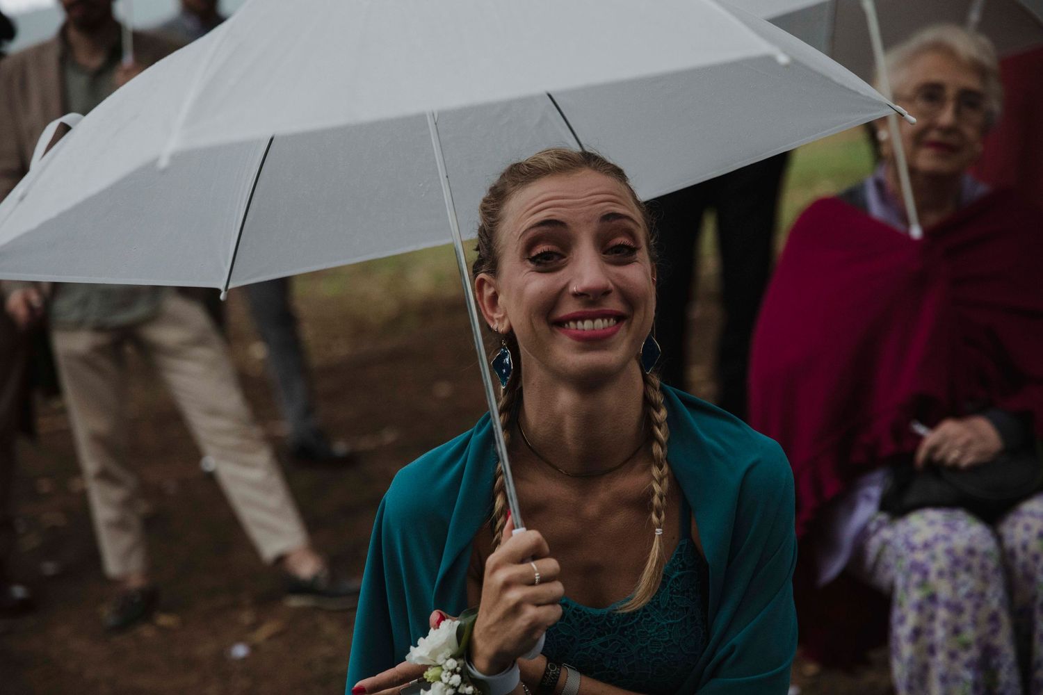 A guest smiles while holding a white umbrella at an outdoor event.