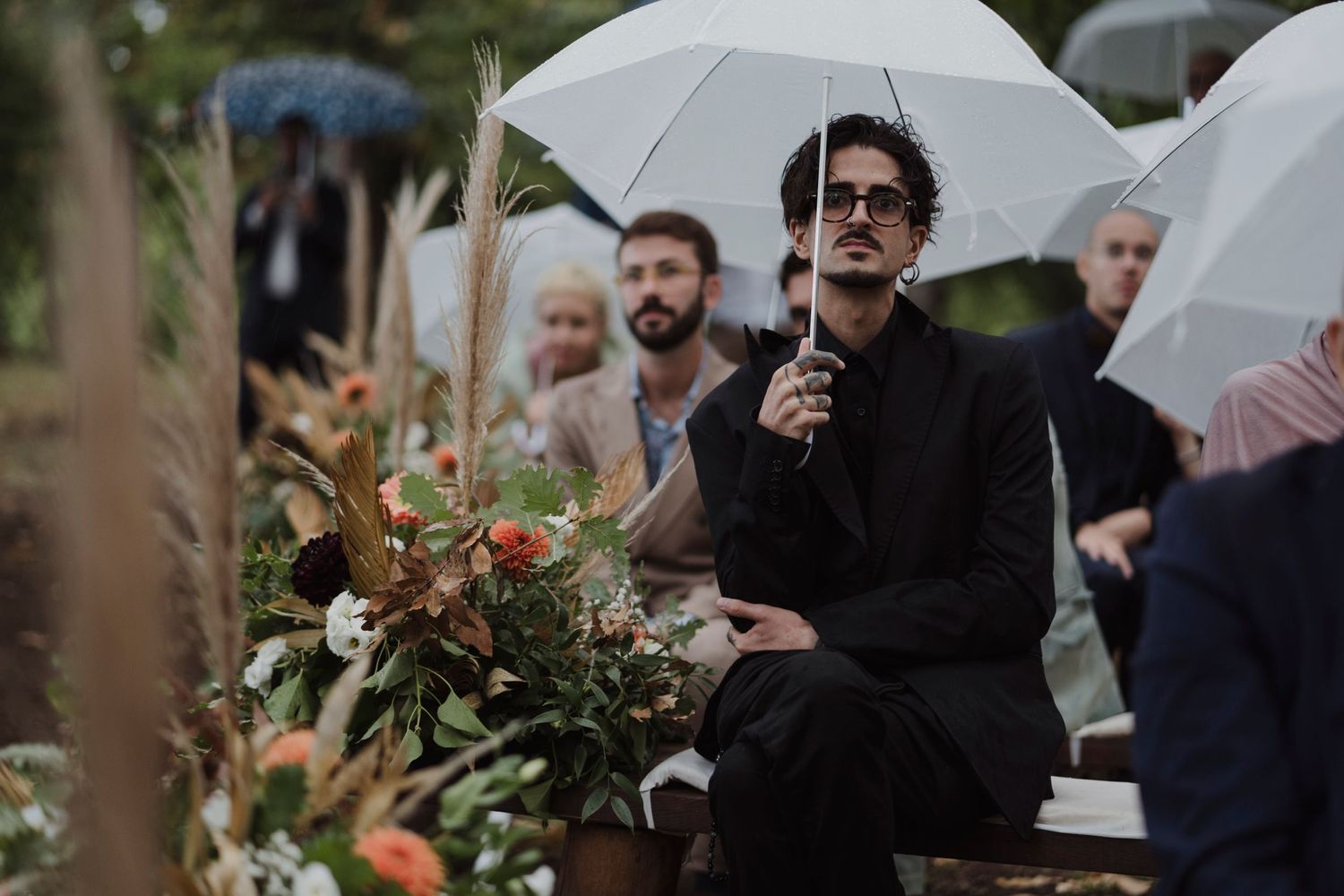 Wedding guests sit under white umbrellas among floral decorations.