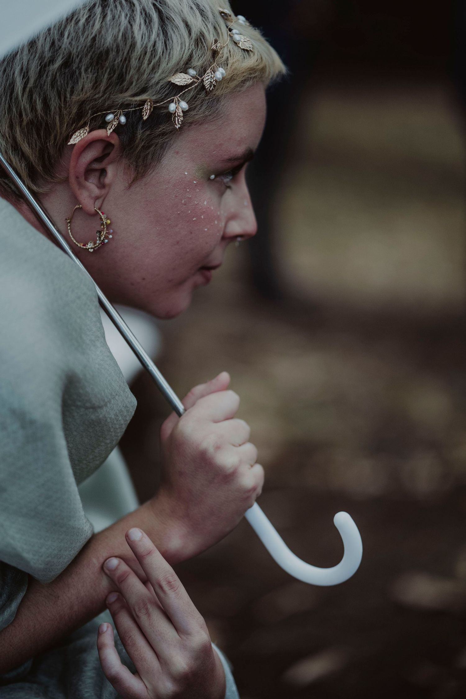 A person wearing a floral crown and holding a white umbrella in moody lighting.