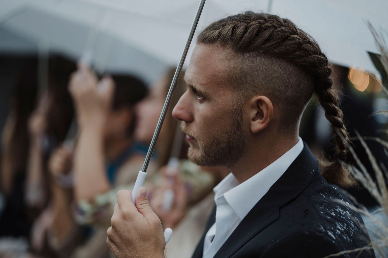 A well-dressed guest holds a white umbrella at an outdoor event in moody lighting.