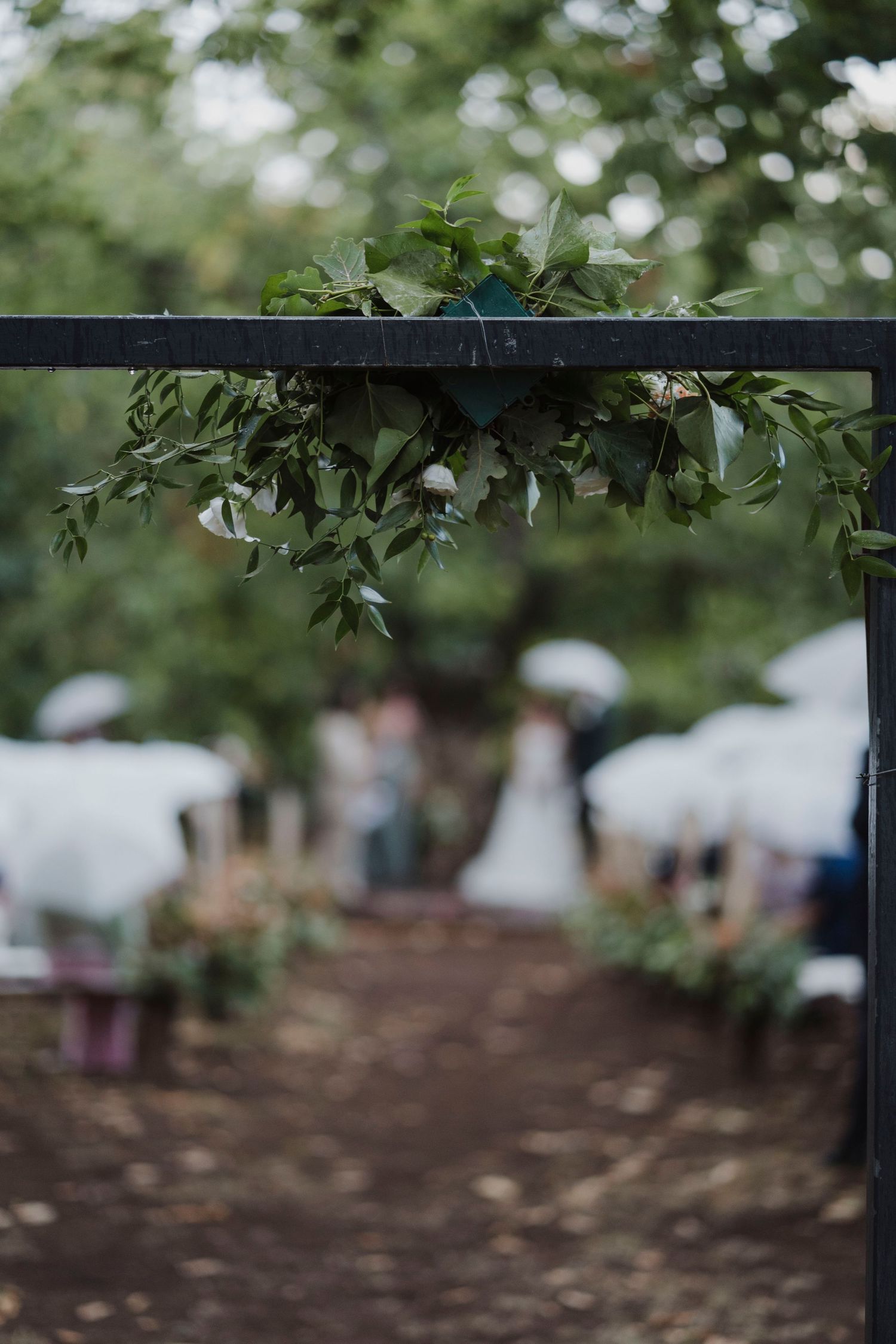 Green foliage decorates a black metal archway at an outdoor wedding venue.