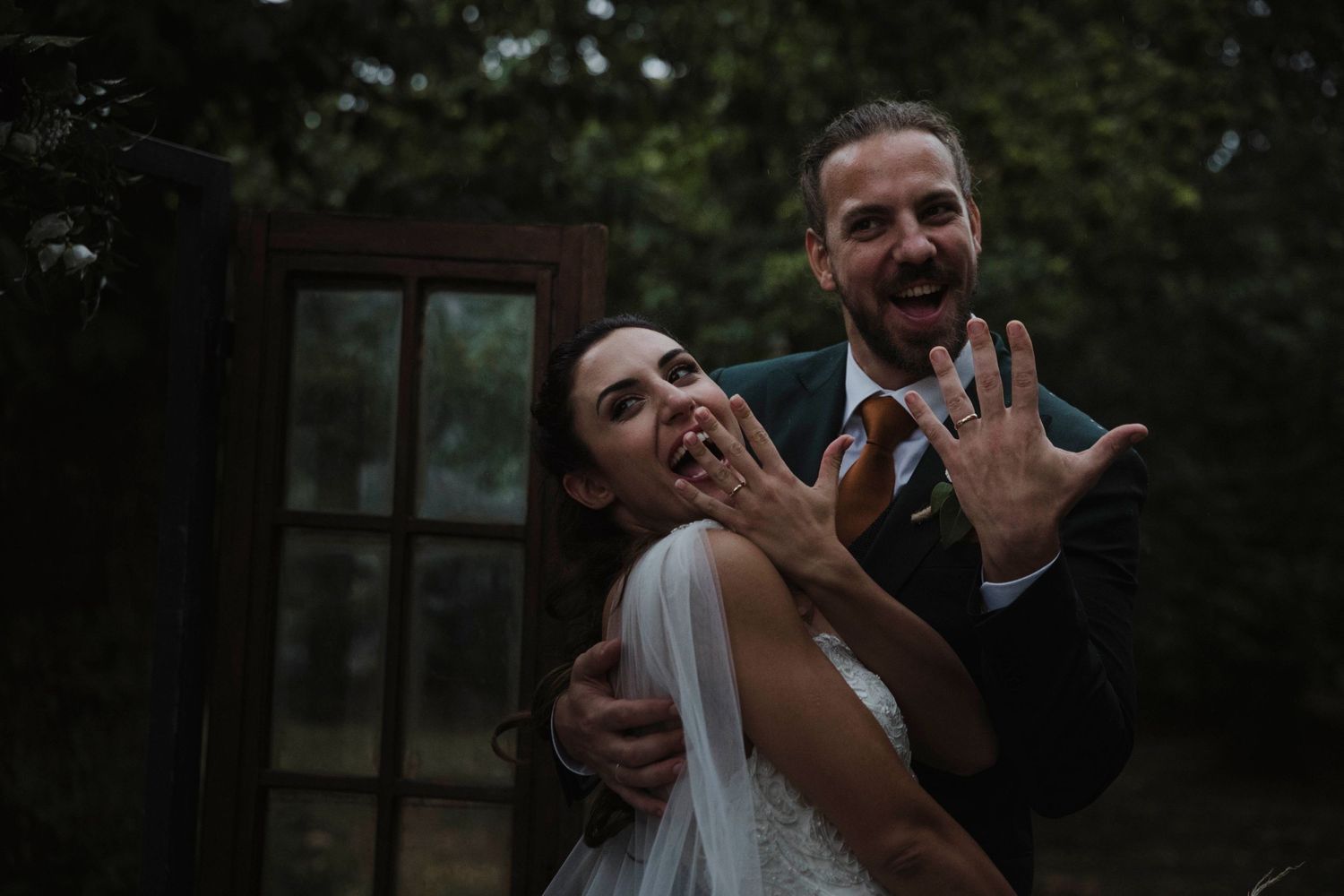 A joyful wedding couple sharing a playful moment outdoors near wooden doors.