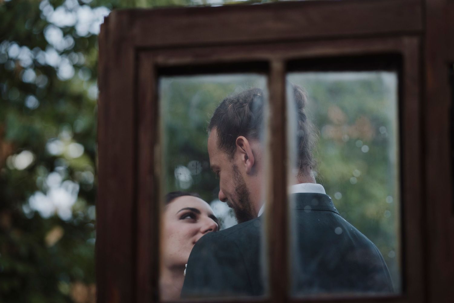 A romantic reflection in an antique wooden window frame shows a couple in an intimate moment.