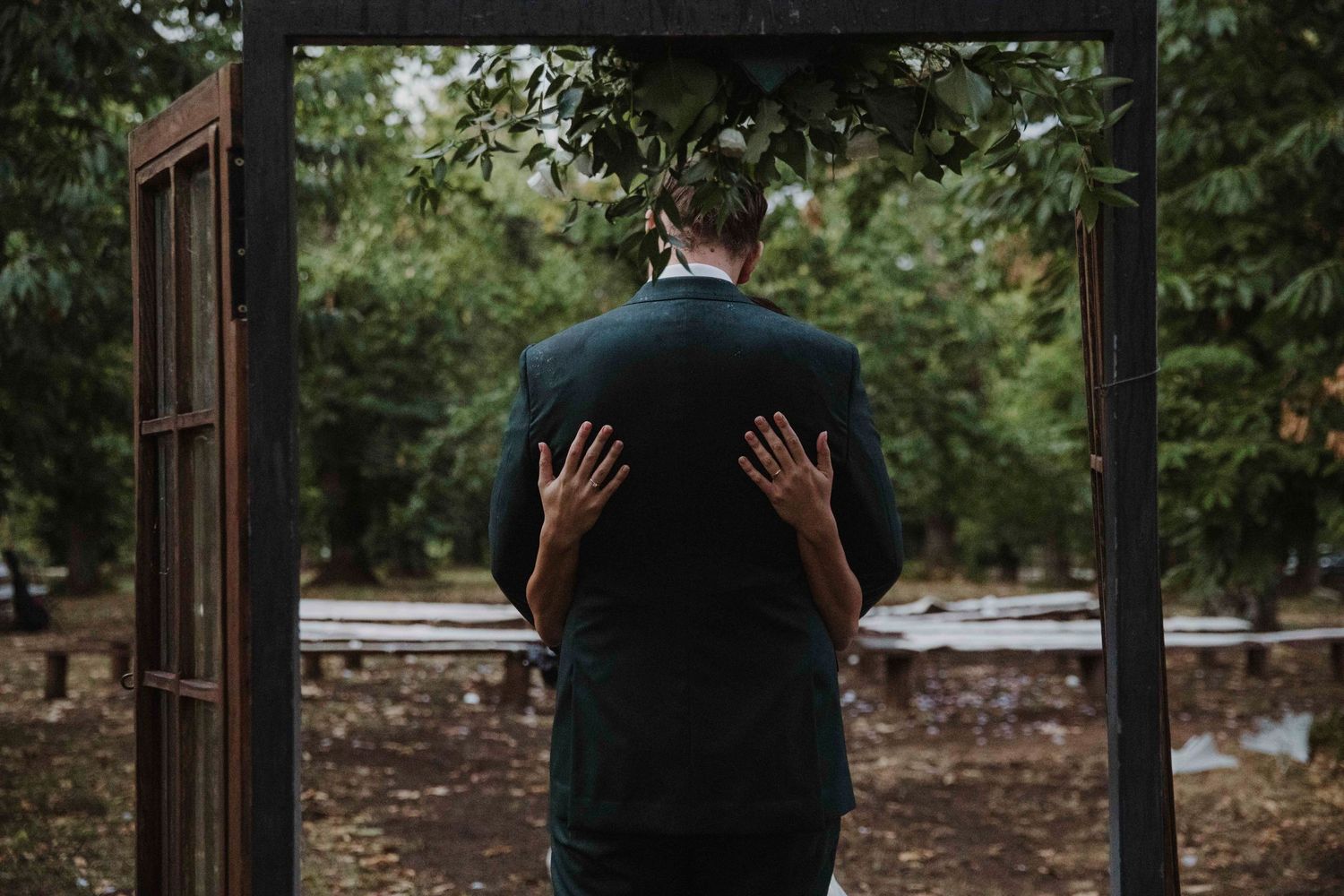 Creative wedding photo showing hands pressed against groom's back through doorway.