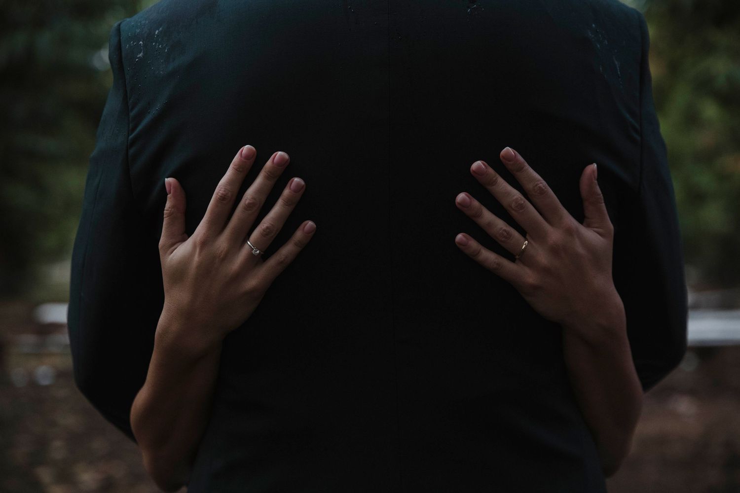 Artistic photo of hands placed on dark suit jacket from behind.