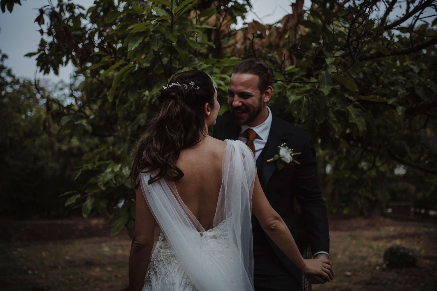 Romantic outdoor wedding moment captured between couple under trees.