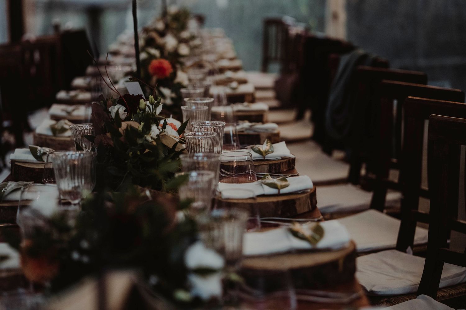 Elegant table settings with floral centerpieces and glassware in moody lighting.