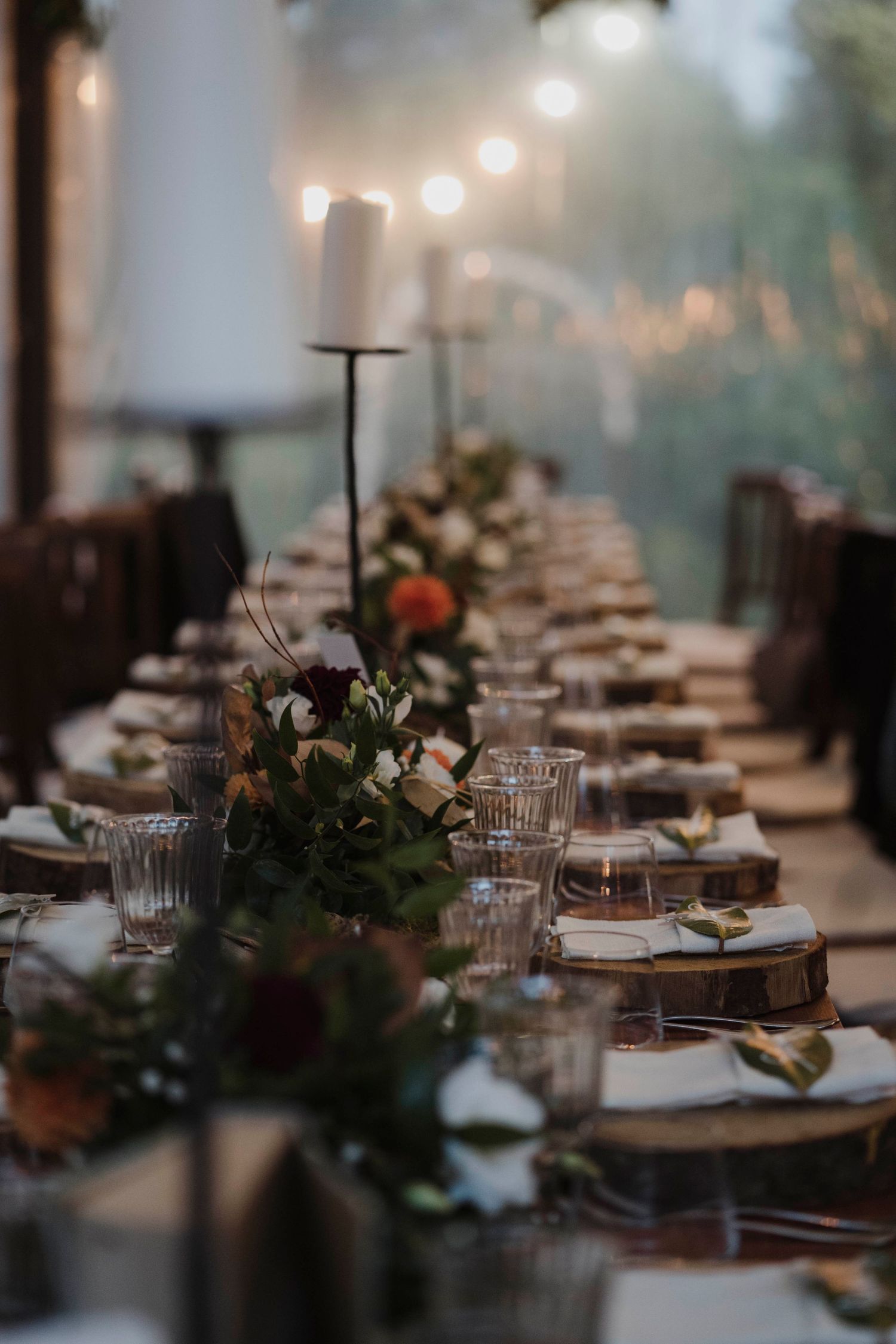 Long dining table set for wedding reception with string lights and greenery centerpieces.