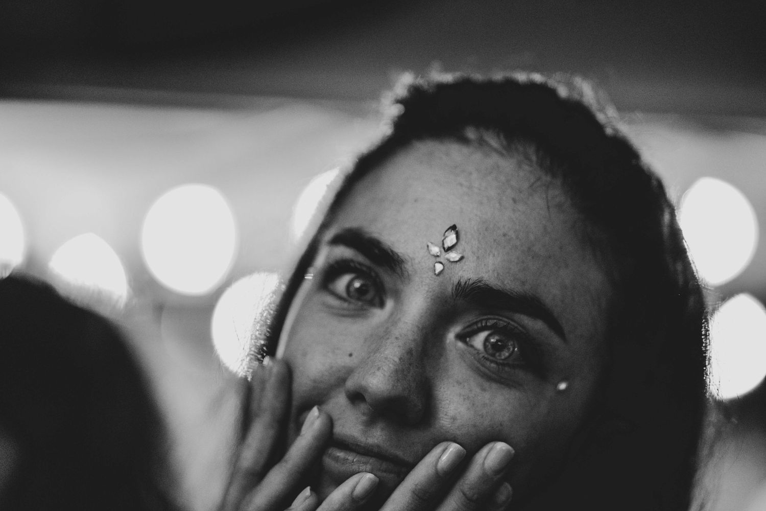 Close-up portrait with bokeh lights and decorative face gems creating a dreamy atmosphere.