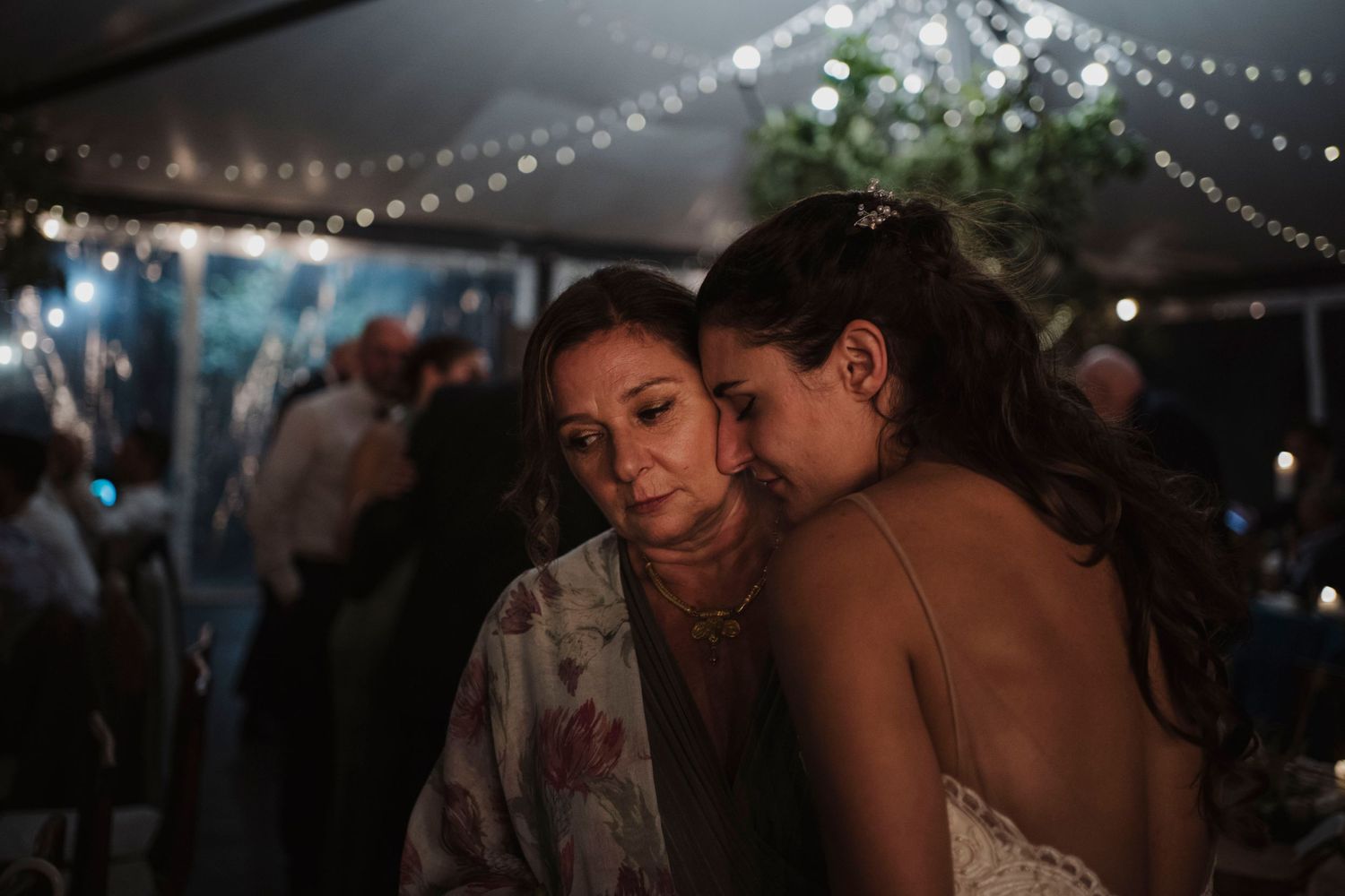 Tender moment between guests during an evening wedding reception under string lights.