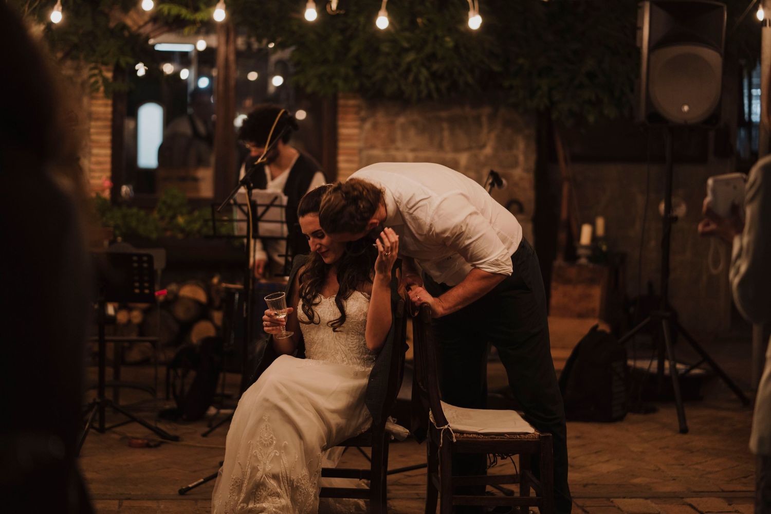 Intimate wedding reception moment captured under warm string lights in rustic venue.