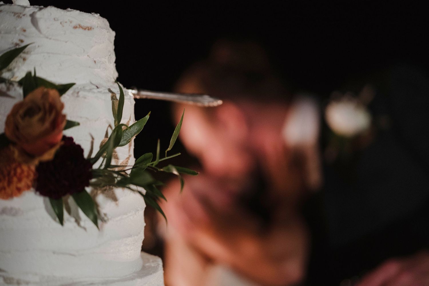 Close-up detail of white wedding cake decorated with red flowers and greenery.