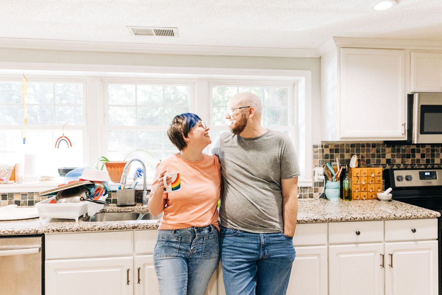 A Charlotte couple smile at each other in their kitchen for family photos