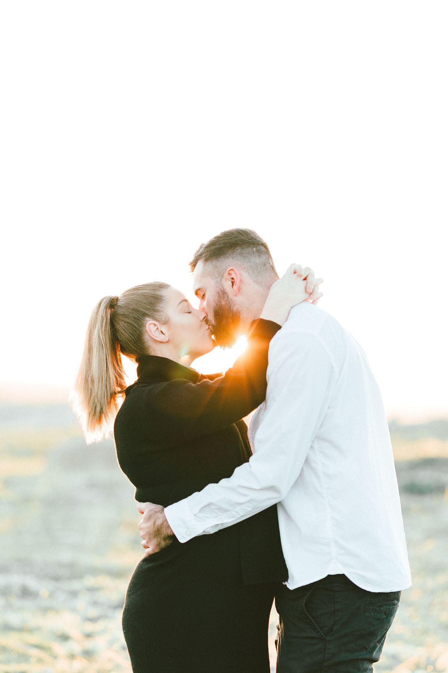 Intimate couple embracing during sunset maternity photo shoot outdoors.