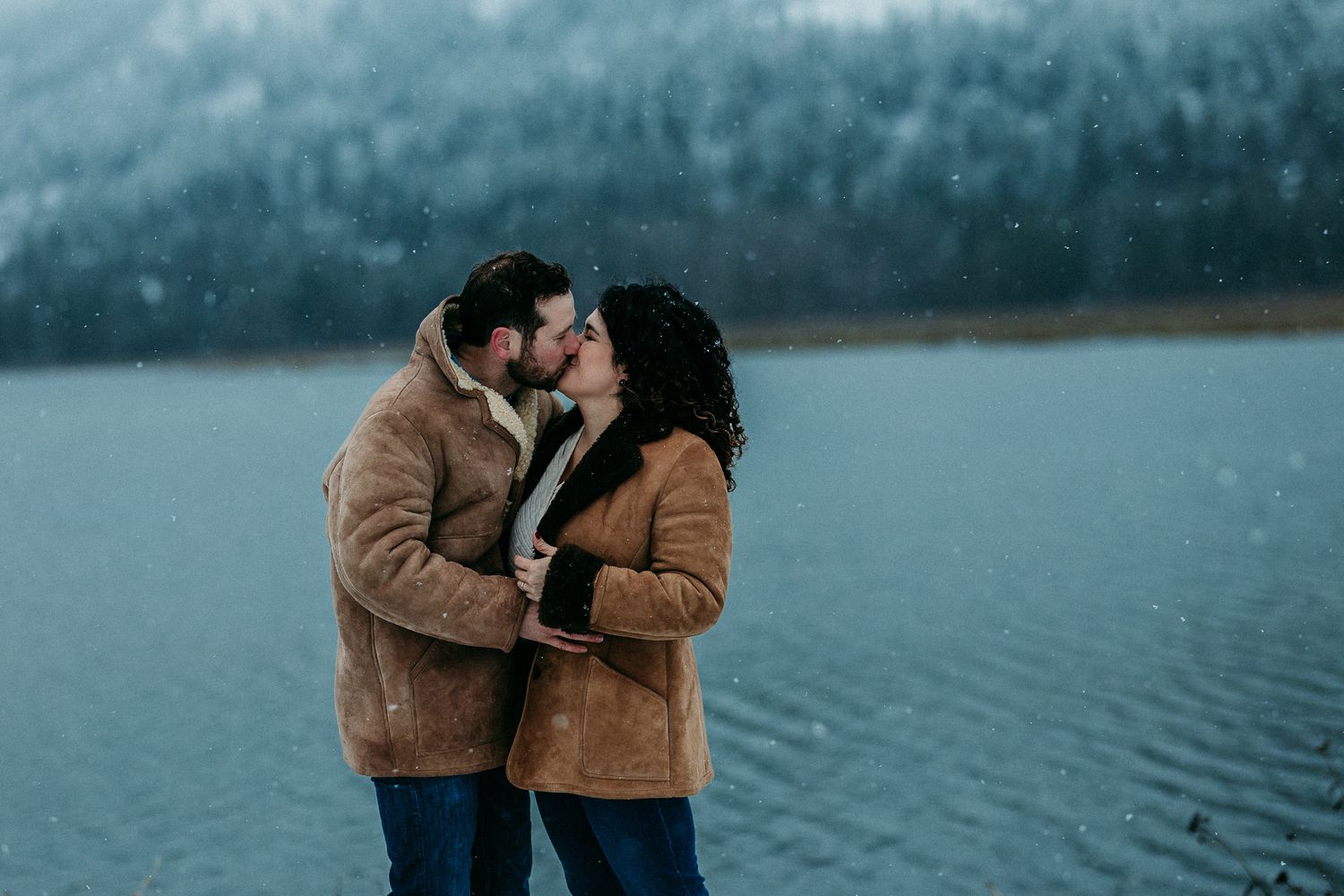 Couple share a kiss by a lake in winter
