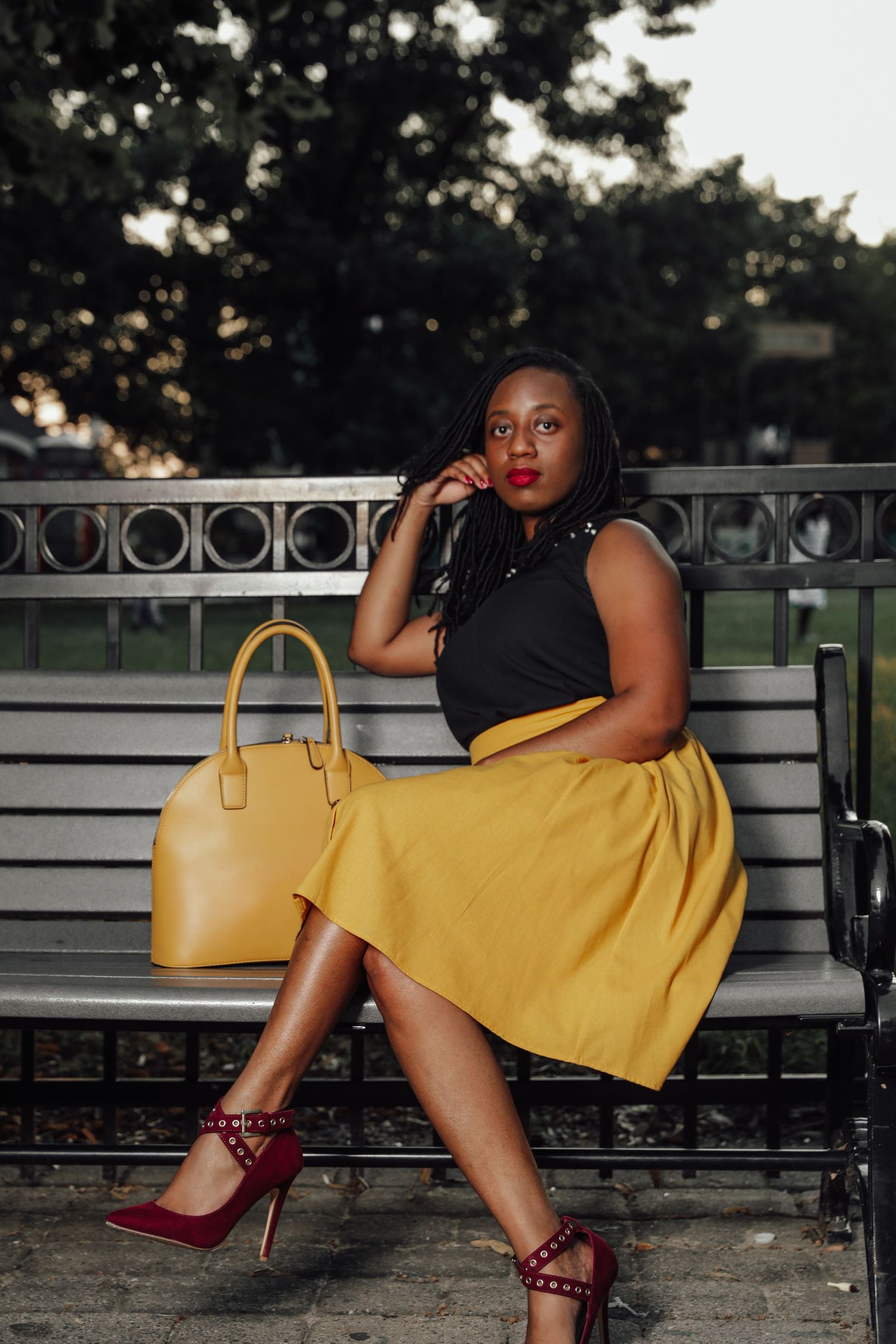 Woman in yellow skirt sitting on bench with yellow handbag.